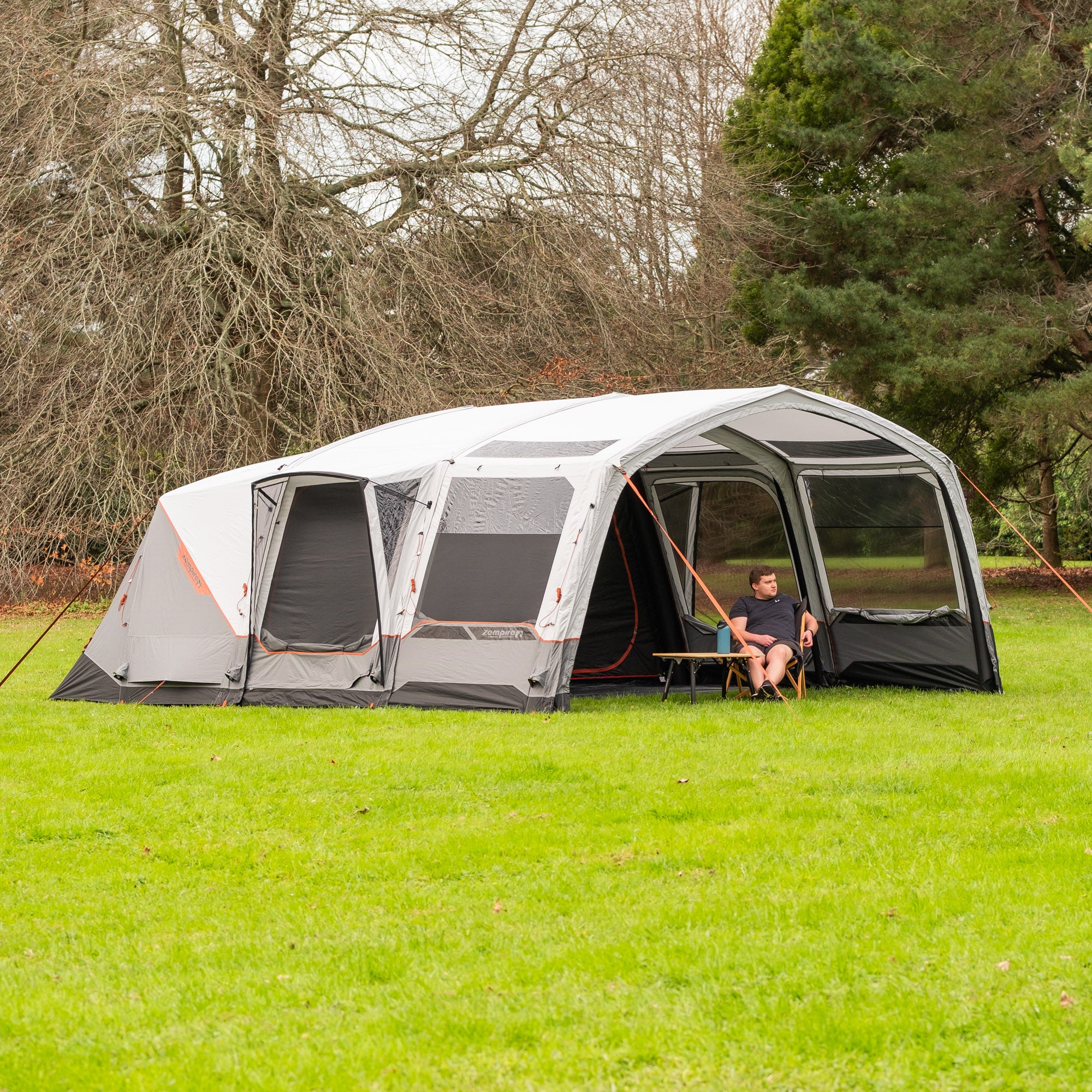 Large Zempire Shapshifter 6 SLA camping tent with attached screen porch on a grassy area with trees in the background