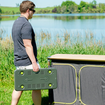 Person setting up a Zempire Stealth-Jet Wide Stove on an outdoor table beside a lake.